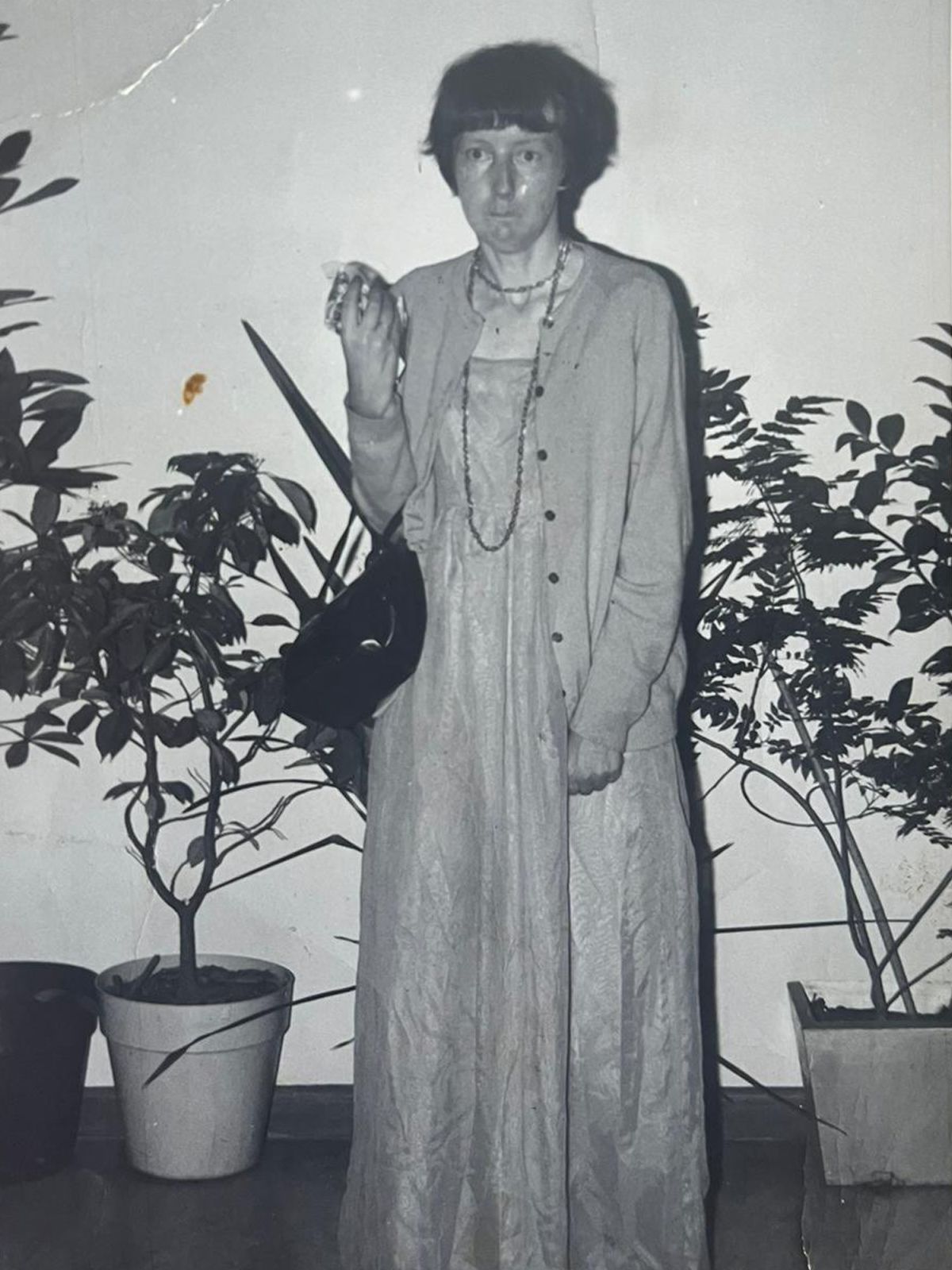 Vintage black and white image of young woman standing holding handbag.